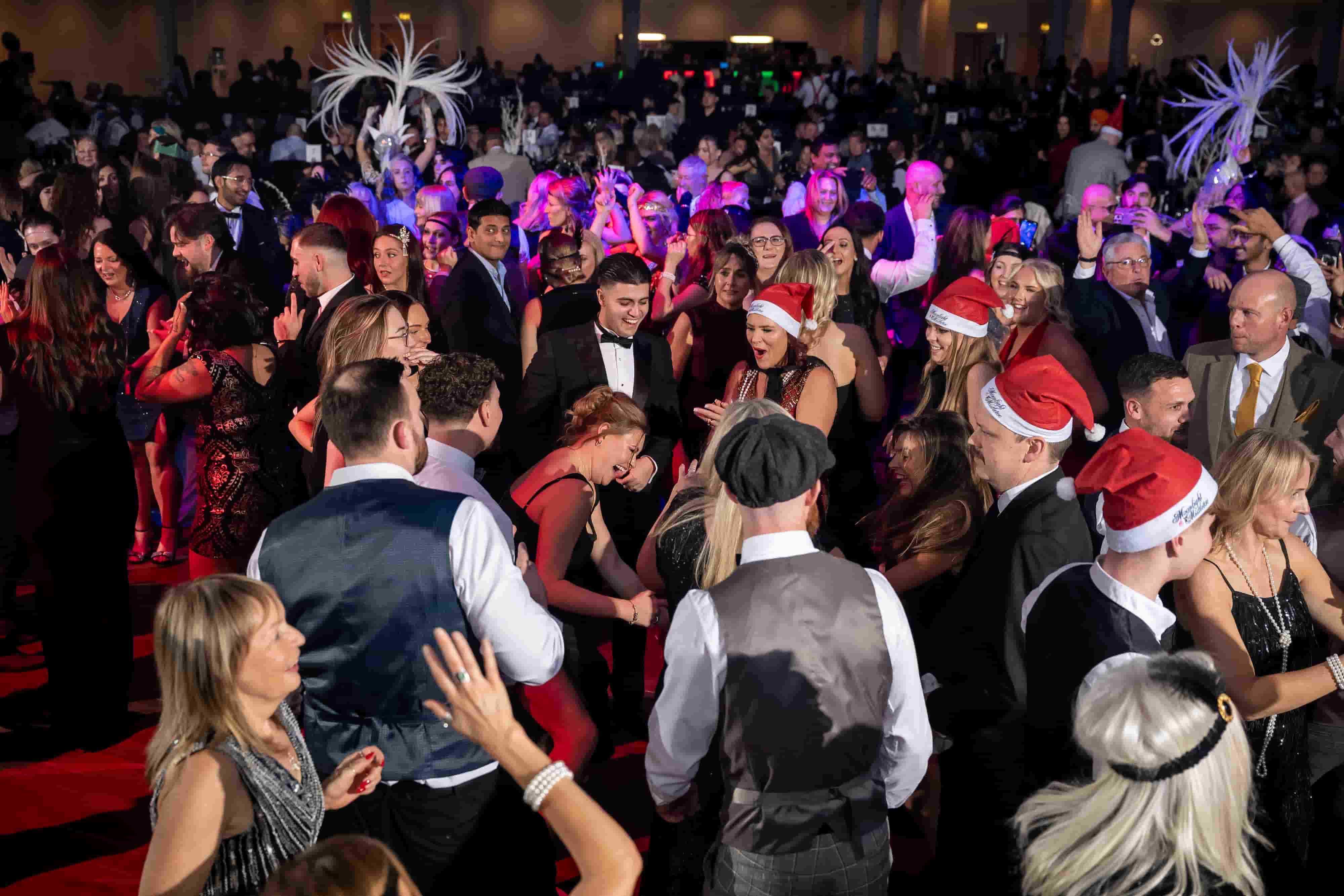 Guests dancing at a Moonlight & Mistletoe shared Christmas party night &mdash; packed dancefloor with Santa hats and production lighting
