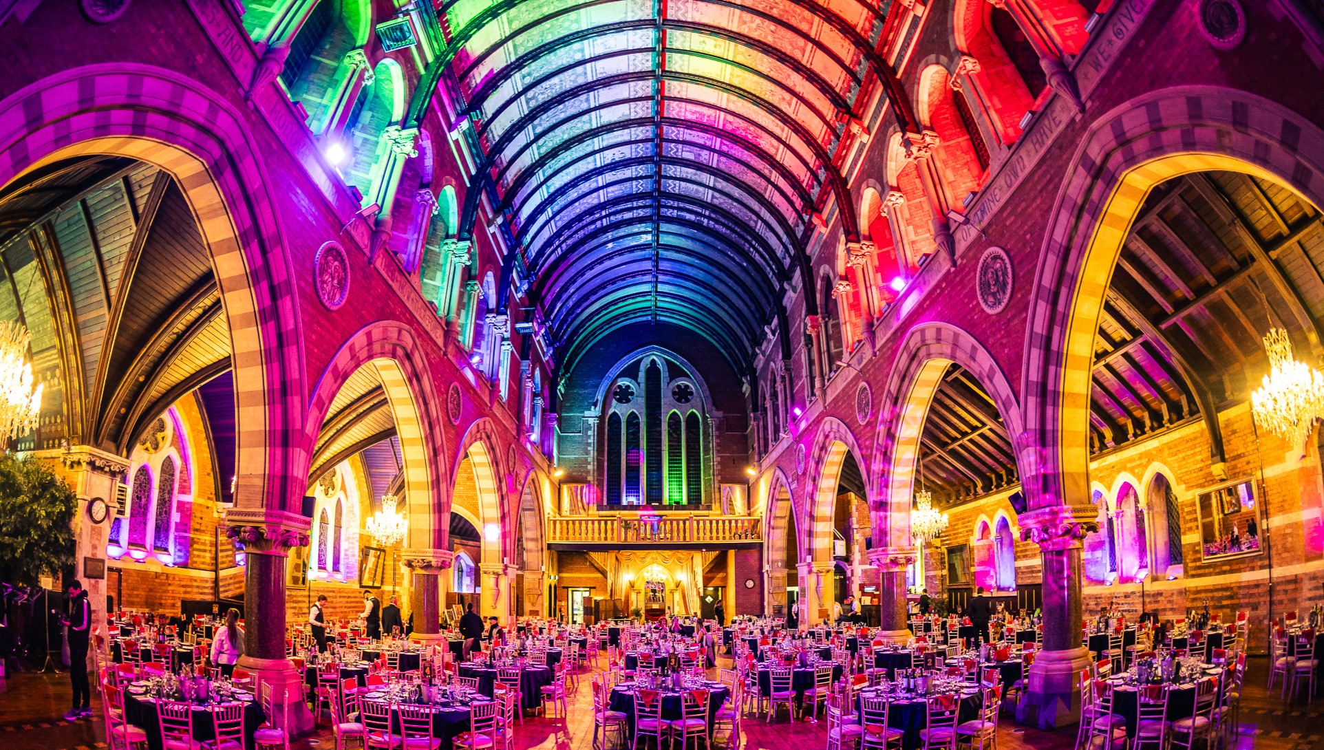 Empire Banqueting Hall Leicester set for a Christmas party night — Grade II-listed Gothic venue with vaulted ceiling lit in rainbow production lighting and round dinner tables